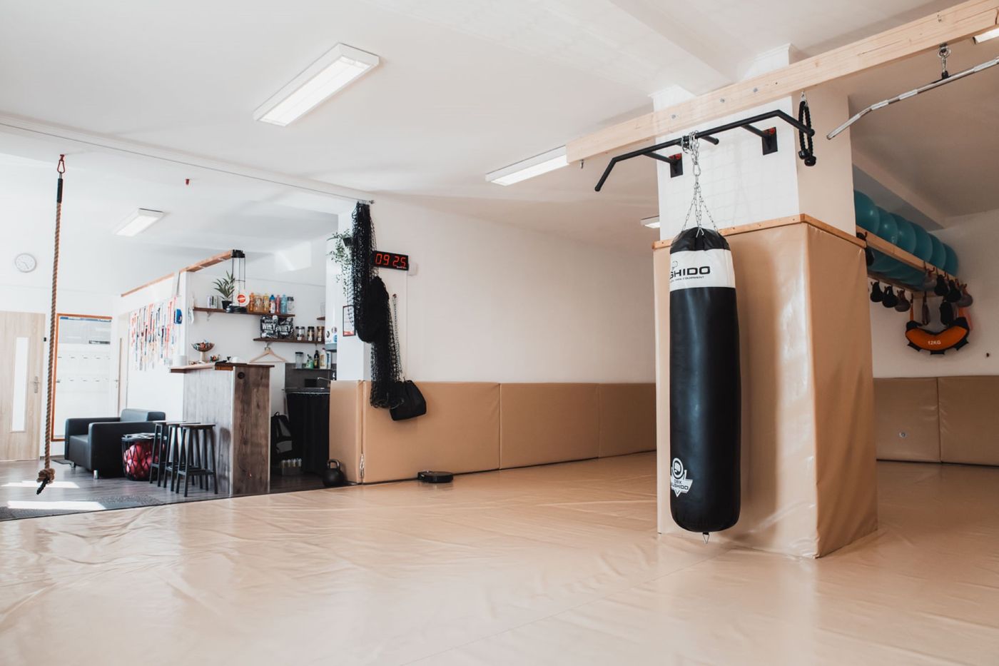 Tělocvična Summit Submission: prázdná tréninková plocha s tatami, uprostřed boxovací pytel, vlevo bar s barovými židlemi a šplhací lano.